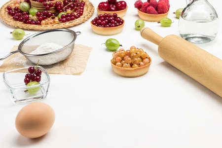 Egg and rolling pin. Flour in sieve. Tartlets with berries. Copy space. White background. Top viewの写真素材
