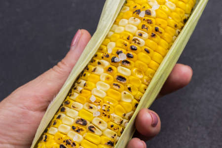 Grilled corn cob in woman's hand. Close-up. Black background.の写真素材