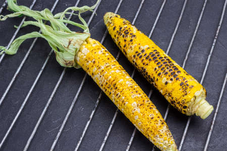 Two grilled corn cob on metal grill grate. Black background. Top viewの写真素材