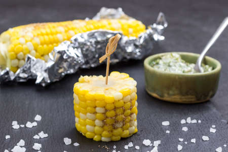 Piece of corn on skewer. Boiled corn in foil. Sauce in bowl. Black backgroundの写真素材