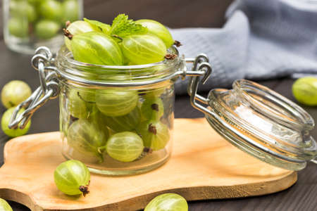 Glass jar with green gooseberries on board. Gray napkin. Dark wooden background. Top viewの写真素材