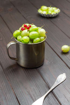Metal mug with green gooseberries and red currants on top. Dark wooden background. Top viewの写真素材