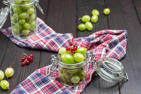 Two glass jars with green gooseberries on check napkin. Dark wooden background. Top viewの写真素材