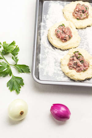 Two onions and twig of parsley. Filling of meat on pieces of raw dough on baking pan. White background. Top viewの写真素材