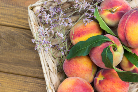 Ripe peaches with green leaves in wicker basket. Wooden background. Flat lay