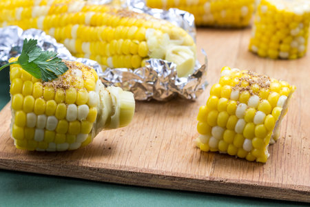 Boiled corn and boiled corn in foil on wooden board. Green background. Close upの写真素材