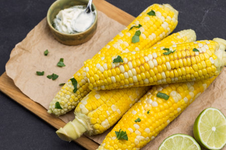 Boiled corn on wooden board. Sauce in bowl. Parsley leaves. Black background. Top viewの写真素材