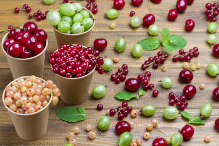 Berries of white and red currants, green gooseberries, cherries in paper caps. Berries and mint leaves on table. Wooden background. Top viewの写真素材