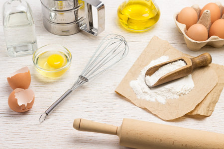 Rolling pin and whisk. Scoop with flour on paper. Chicken shells and eggs in container. Water in...