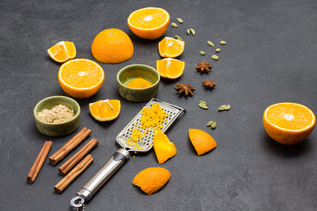 Grated orange peel on grater. Sliced orange and dry ginger, cinnamon sticks and star anise on table....