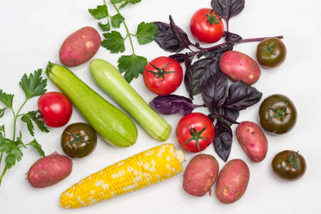 Set of vegetables and sprigs of basil and parsley. Potatoes, cob of corn, tomatoes and zucchini on white. Flat layの写真素材