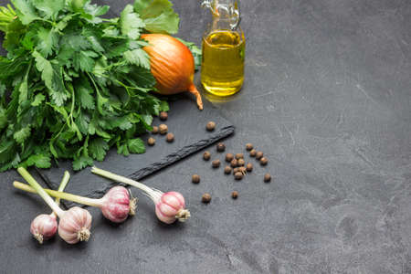 Heads of garlic, allspice, oil and bunch of parsley on black. Vegetable background. Copy space. Top view.の写真素材