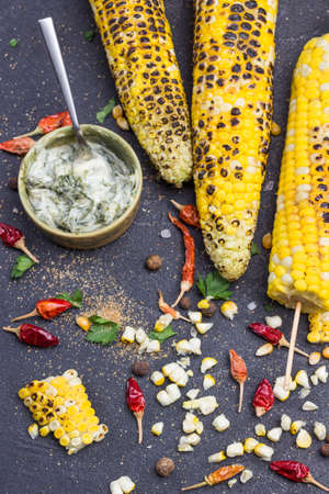 Grains and pods of dry red pepper on table. Bowl of sauce. Grilled corn cobs, chopped corn. Black background. Top view.の写真素材