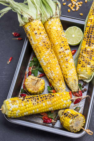 Grilled corn and dried red pepper pods on pallet. Black background. Top viewの写真素材