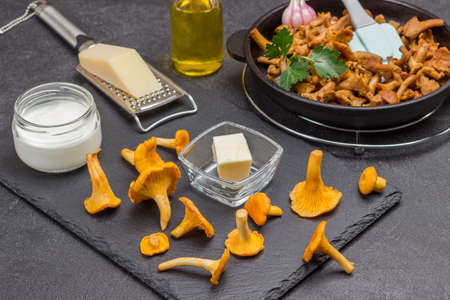 Raw chanterelle mushrooms, butter, grated cheese. Fried chanterelles in pan. Black background. Top viewの写真素材