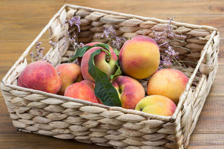 Ripe peaches with green leaves in wicker basket. Wooden background. Top viewの写真素材