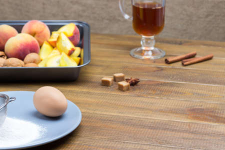 Ripe peaches and walnuts in metal tray. Flour, sieve and egg on gray plate. Copy space. Wooden background.の写真素材
