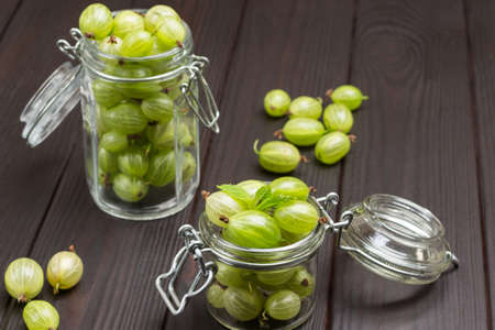 Green gooseberries in two glass jars. Wooden background. Top view.の写真素材