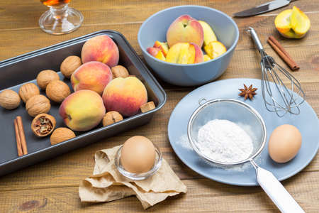 Ripe peaches and walnuts in metal tray. Flour, sieve and egg on gray plate. Sliced peaches in gray plate. Wooden background. Top viewの写真素材