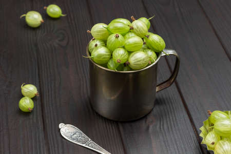 Green gooseberries in metal mug. Berry on table. Top view. Wooden background.の写真素材