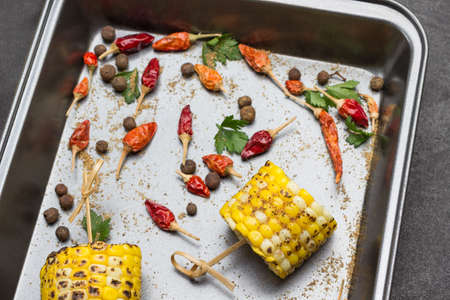 Grilled corn pieces on skewers on tray. Dry pods of red pepper. Top viewの写真素材