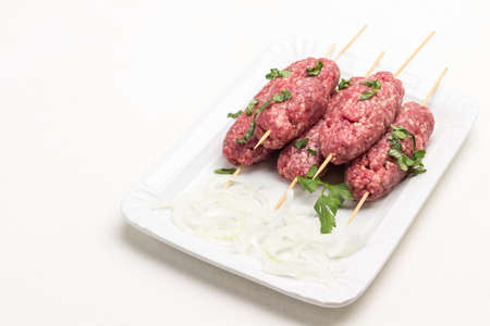 Raw minced meat on wooden skewers and chopped onion rings on white plate. White background.の写真素材