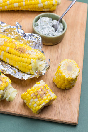 Boiled corn and boiled corn in foil on wooden board. Green background. Close up