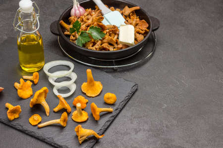 Raw chanterelle mushrooms, onions and oil in bottle on black tray. Fried chanterelles in pan. Sschzn yzfsu. Black background. Top viewの写真素材