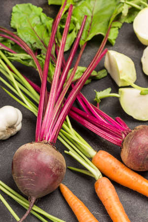 Fresh beets with tops. Carrots with stalks and chopped kale turnip cabbage. Black background. Top viewの写真素材
