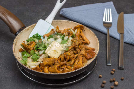 Fried chanterelles in pan. Fork and knife on gray napkin. Black background. Top viewの写真素材