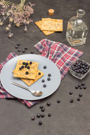 Biscuits and blueberries on gray plate on checkered napkin. Bottled water. Blueberries in glass bowl. Spoon is on plate. Black background. Top viewの写真素材
