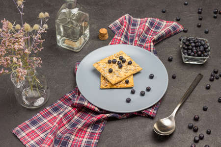 Gray plate with cookies and blueberries on checkered napkin. Bottled water. Blueberries in glass bowl. The spoon is on table. Black background. Top viewの写真素材