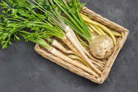 Parsley with leaves and roots, celery tuber with leaves in wicker basket. Flat lay. Copy space. Black backgroundの写真素材
