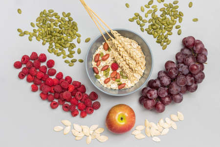Nuts, oatmeal and wheat spikelets in gray bowl. Raspberries and bunch of grapes, pumpkin seeds on table. Flat lay. Gray backgroundの写真素材