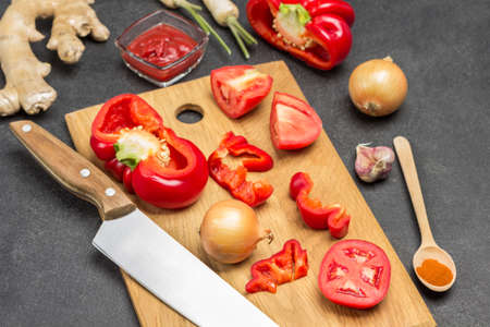 Red pepper, tomato and knife on cutting board. Ginger root, onion and spoon on table. Black background. Top viewの写真素材