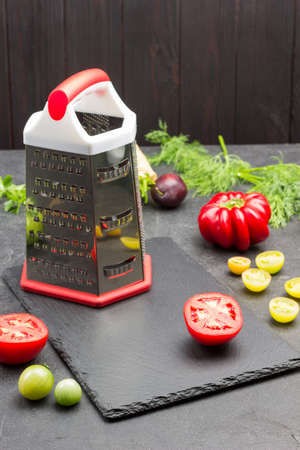 Grater and slices of red tomato on cutting board. Pepper and dill on table. Black background. Top viewの写真素材