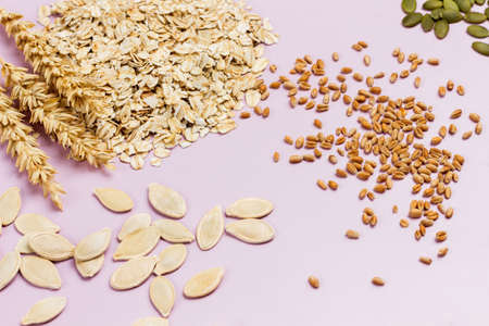 Oat flakes, spikelets and grains of wheat. Pumpkin seeds. Flat lay. Pink backgroundの写真素材