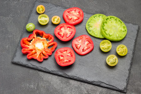 Slices of green and red tomatoes on cutting board. Copy space. Black background. Flat layの写真素材