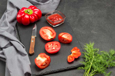 Sliced red tomatoes and knife on cutting board. Sprig of dill and gray napkin on table. Black background. Top viewの写真素材