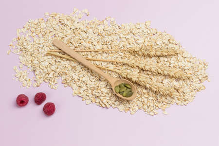 Wheat spikelets on oatmeal. Pumpkin seeds in wooden spoon. Flat lay. Pink backgroundの写真素材