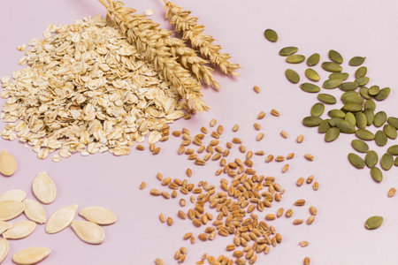 Wheat spikelets and oat flakes. Pumpkin seeds and wheat grains on table. Flat lay. Pink backgroundの写真素材