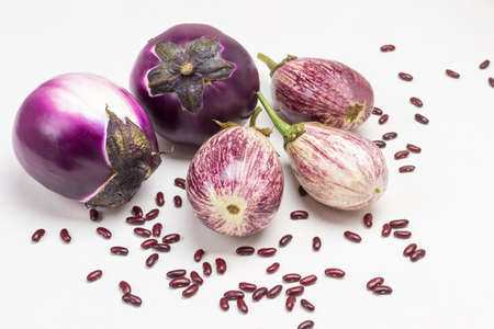 Two purple eggplants and three striped eggplants. Beans on table. Top view. White background.の写真素材