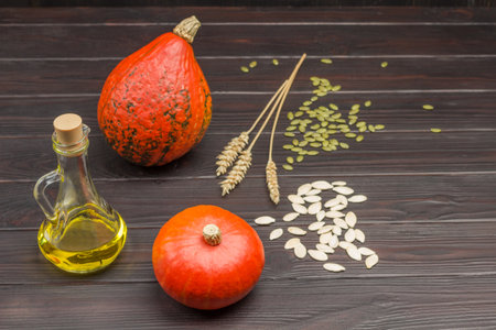 Pumpkins, oil in bottle and seeds on table. Sprigs of wheat. Wooden background.の写真素材