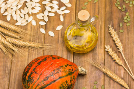 Red pumpkin and bottle of oil. Pumpkin seeds and spikelets of wheat on table. Wooden background. Flat lay.の写真素材