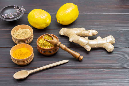 Raw ginger root. Dry ginger powder, pollen in bowls. Two whole lemons. Wooden background. Top view.の写真素材