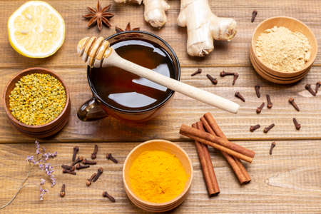 Honey in a glass bowl. Flower pollen, dry ginger and turmeric powder in wooden bowls. Wooden background. Top viewの写真素材
