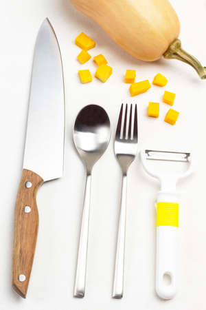 Kitchen knife, spoon, fork and peeler. Sliced pumpkin slices. Pumpkin with dry stem. White background. Flat layの写真素材