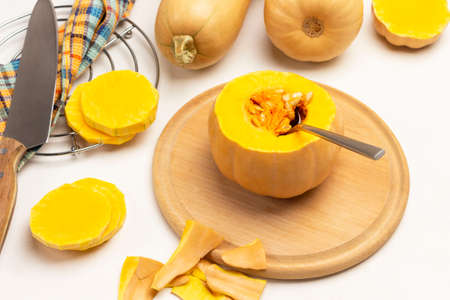 Spoon in pumpkin pulp on cutting board. Peeling pumpkin on table. Knife on napkin, pumpkin slices on metal stand. White background. Flat layの写真素材