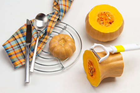Orange pumpkin and peeler. Knife and spoon on napkin. Piece of pumpkin on metal stand. White background. Top view.の写真素材