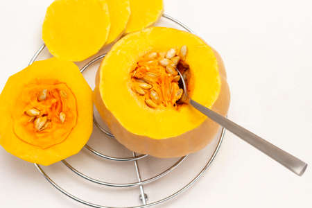 Sliced pumpkins on metal stand. Spoon in pumpkin pulp. White background. Flat layの写真素材